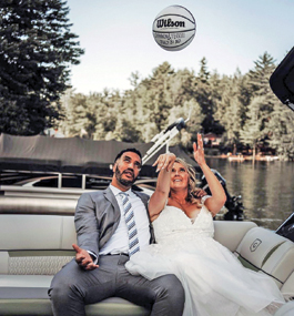 A bride and groom are seated outside side-by-side; the woman is tossing a white basketball in the air