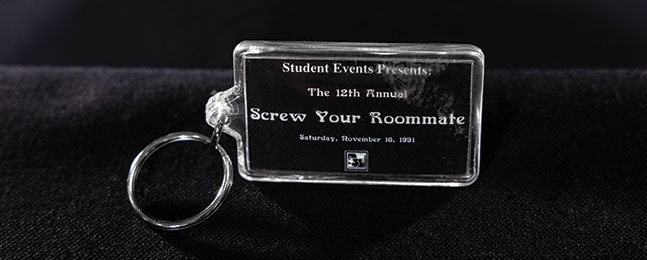 A photo of a clear plastic keychain labeled "Student Events Presents / The 12th Annual / Screw Your Roommate / November 16, 1991."