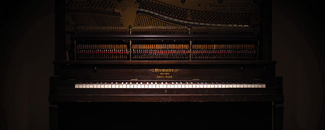 A shadowy photo of a brown upright piano.