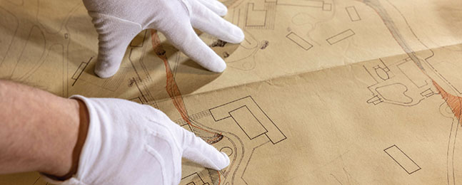 White-gloved hands point to an area on a schematic drawing.
