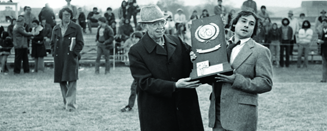 An unidentified man hands Coach Mike Coven a heavy trophy.