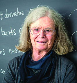 A headshot of a smiling woman leaning against a blackboard.