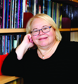 Headshot of a smiling woman leaning her head against her hand in front of a bookcase.