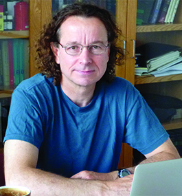 Headshot of man with curly brown hair wearing a blue T-shirt.