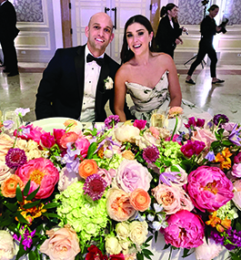 A man and woman smile behind a table filled with flowers