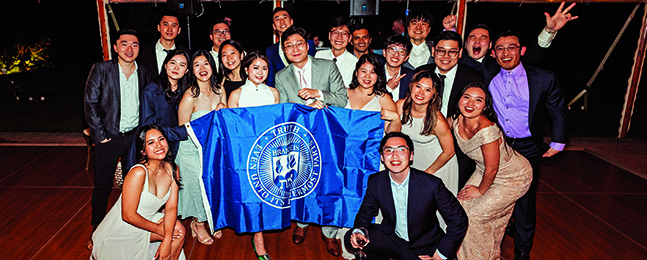 A group of people, including the bride and groom, stand behind a Brandeis banner