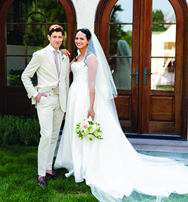 A bride and groom, both wearing white, pose casually