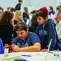 Two young boys wearing Brandeis gear look at at a mobile phone together