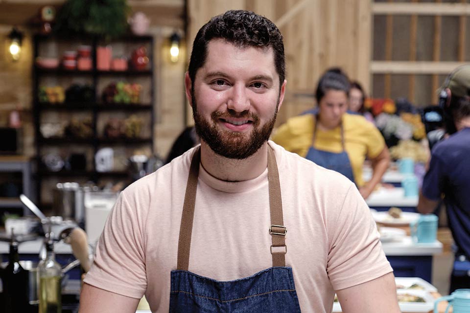 Brad Mahlof wearing a denim apron, with four plates of cod cakes, rice and vegetables between his hands on a counter.