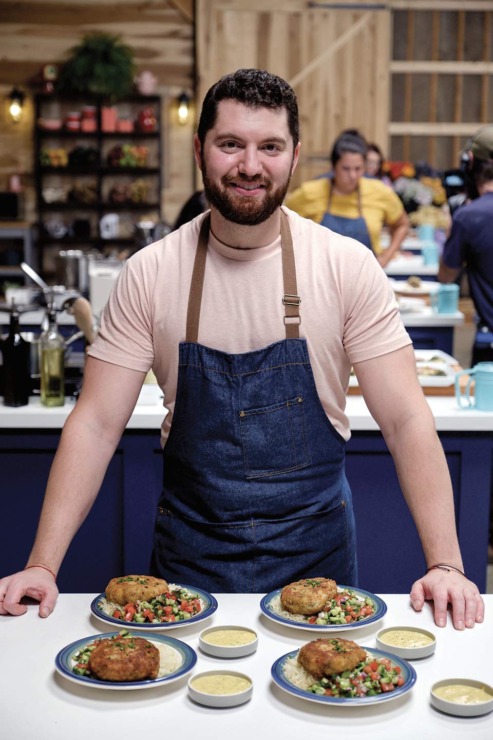 Brad Mahlof wearing a denim apron, with four plates of cod cakes, rice and vegetables between his hands on a counter.
