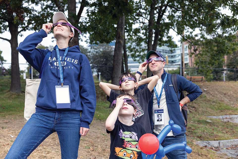 A family wearing solar eclipse glasses looks up at the sky