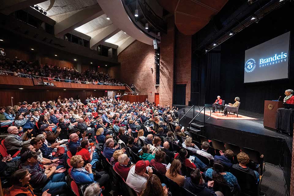 Panelists sit on a stage facing an auditorium full of people