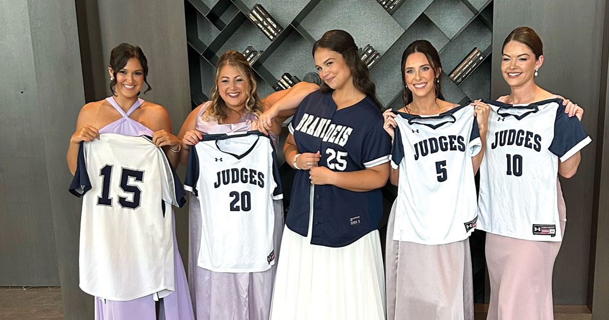 A bride wears a Brandeis jersey while four bridesmaids hold up Brandeis jerseys