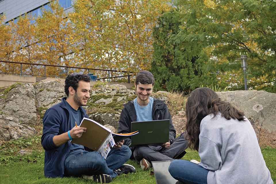 Three people sitting on the grass on the Brandeis campus