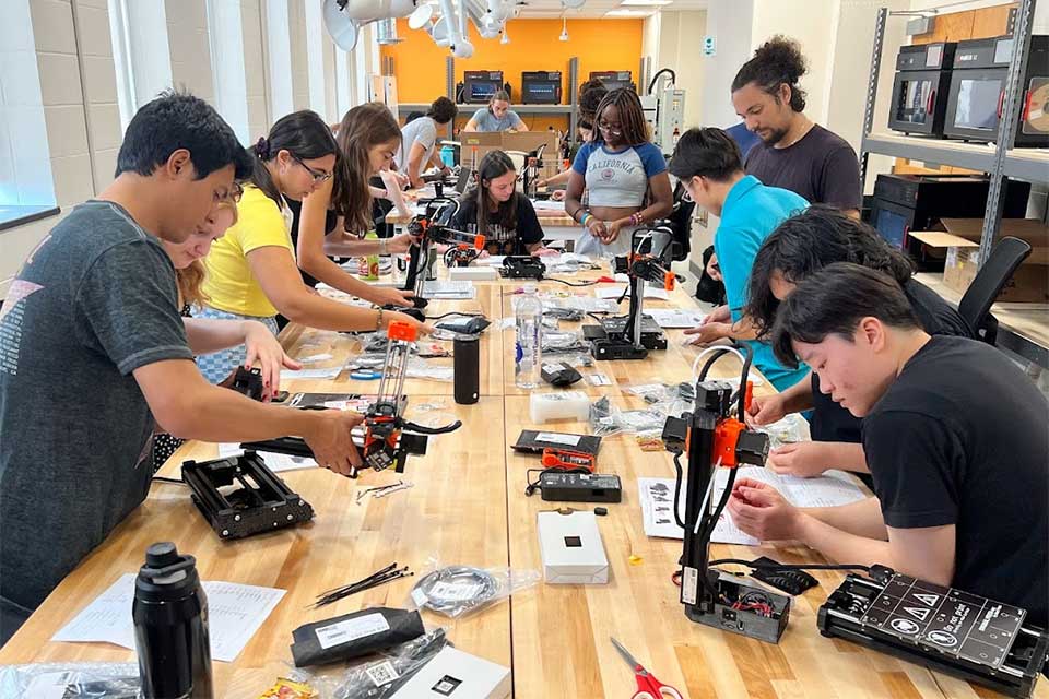 Many engineering students work on projects at a long table.
