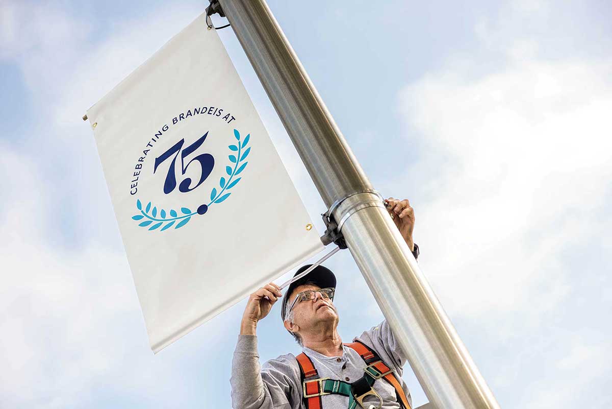 A facilities staff member puts the 75th banner up on a lightpost