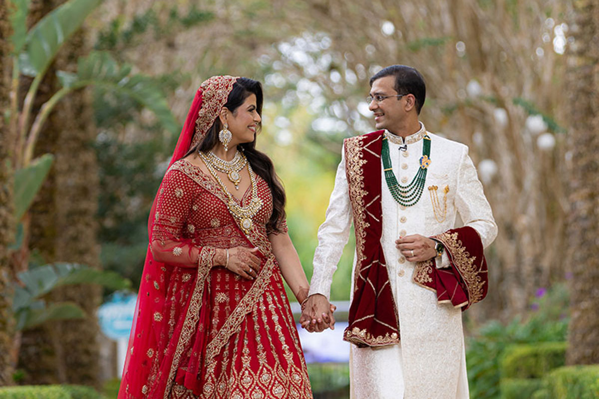 A bride and groom walk down a path together holding hands.