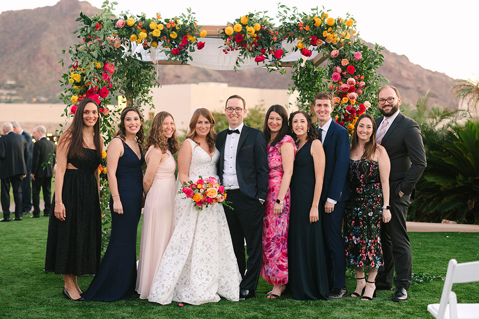A wedding party stands together outside, smiling.