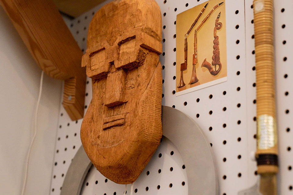 A carved wooden face hangs on the wall of Mairson's workshop next to various tools.