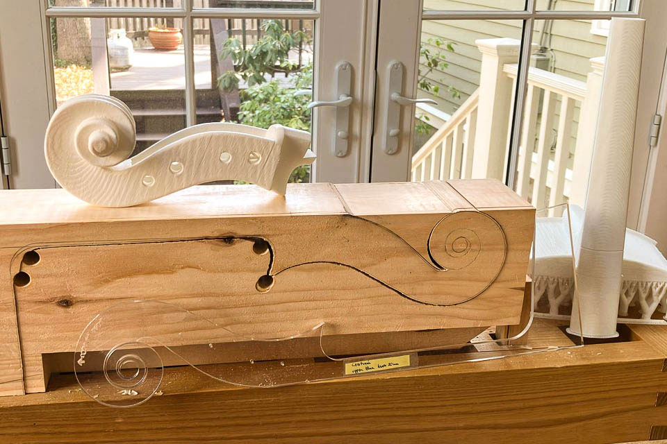 A wooden block with the beginning shape of a cello's scroll carved into it.