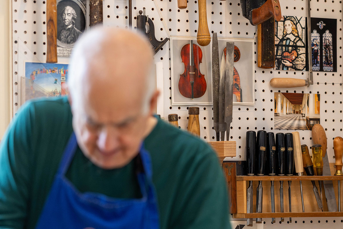 Mairson cuts a piece of wood with a tool in his workshop.