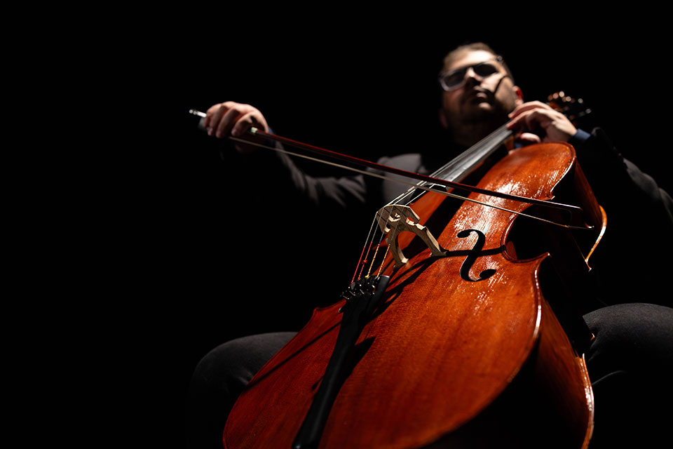 A person plays a cello on a dark stage.