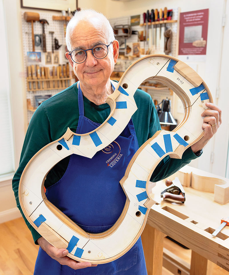 Harry Mairson standing in his workshop holding the body of a cello.