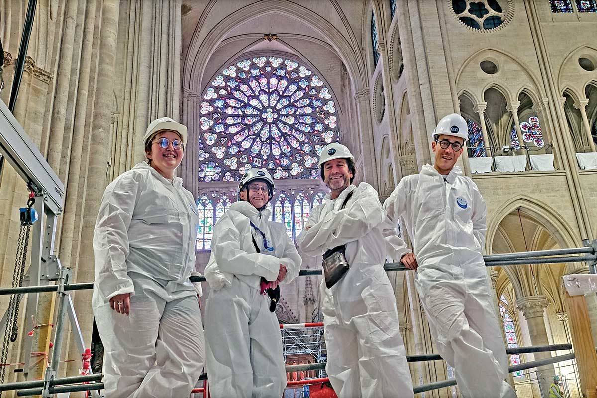 Four people wearing white zip-up suits and hard hats smiling inside Notre Dame.