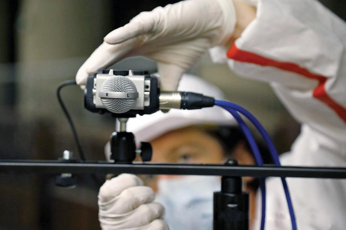 A person wearing a white protective suit adjusting a piece of sound equipment.