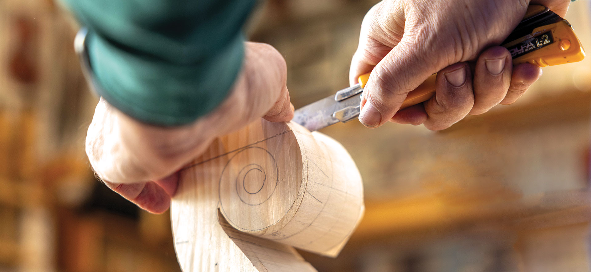 Hands carving a cello's scroll with a knife.