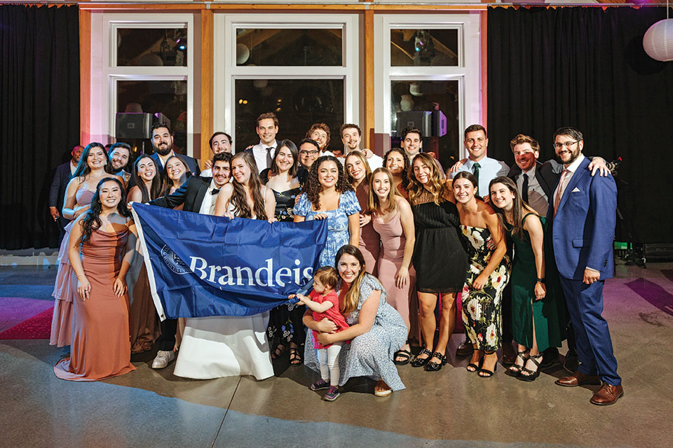 Rachel Goldstein, Tazio De Tomassi, and friends hold up a Brandeis flag at their wedding.