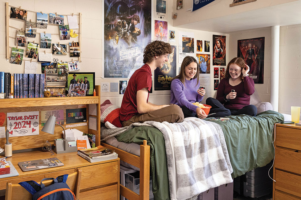 Students sitting on a bed in a dorm room playing a card game.