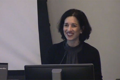 A speaker smiles behind a podium in a classroom.