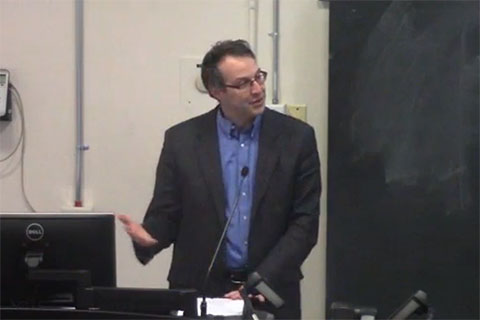 A speaker talks behind a podium in a classroom.