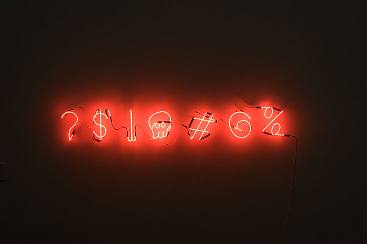 A red neon sign made up of several symbols, including a question mark, a skull, and an at sign.