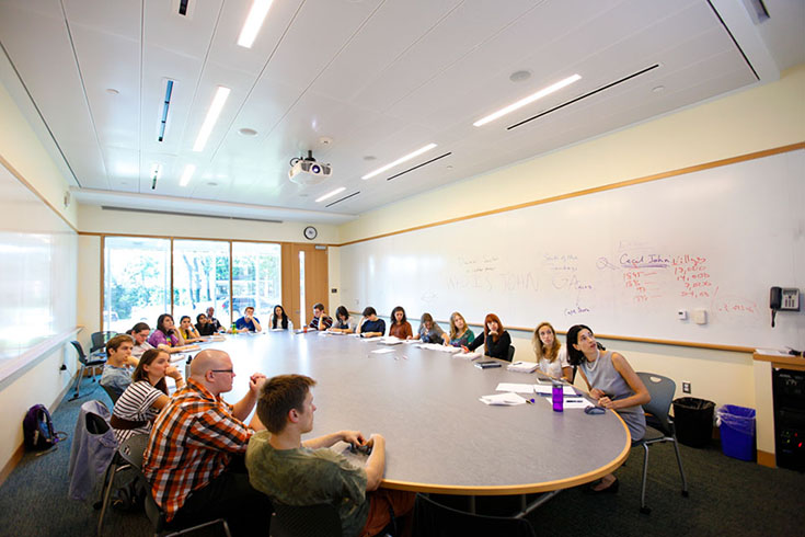 A group of students sit around a circular table inside a classroom.