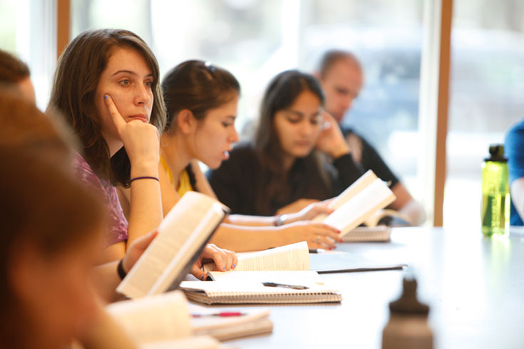 Several people sit at a table, each holding a reading packet.