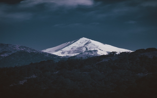 A snow-capped mountain against darker peaks