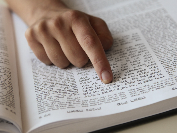 A person's fingers on the pages of a book written in Hebrew.
