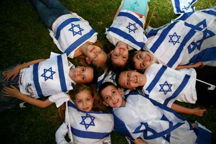 6 children lying in a circle, holding Israeli flags