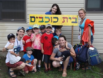 Kids at camp posing under a sign in Hebrew
