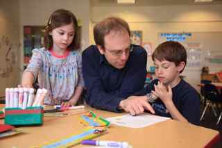 An adult instructs 2 small children sitting at a table