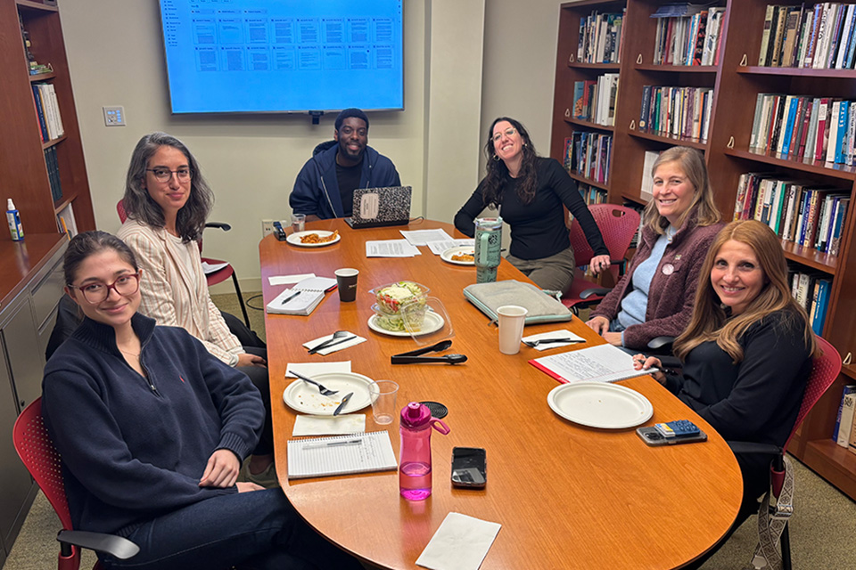 Group around a table with a TV screen on in the background.
