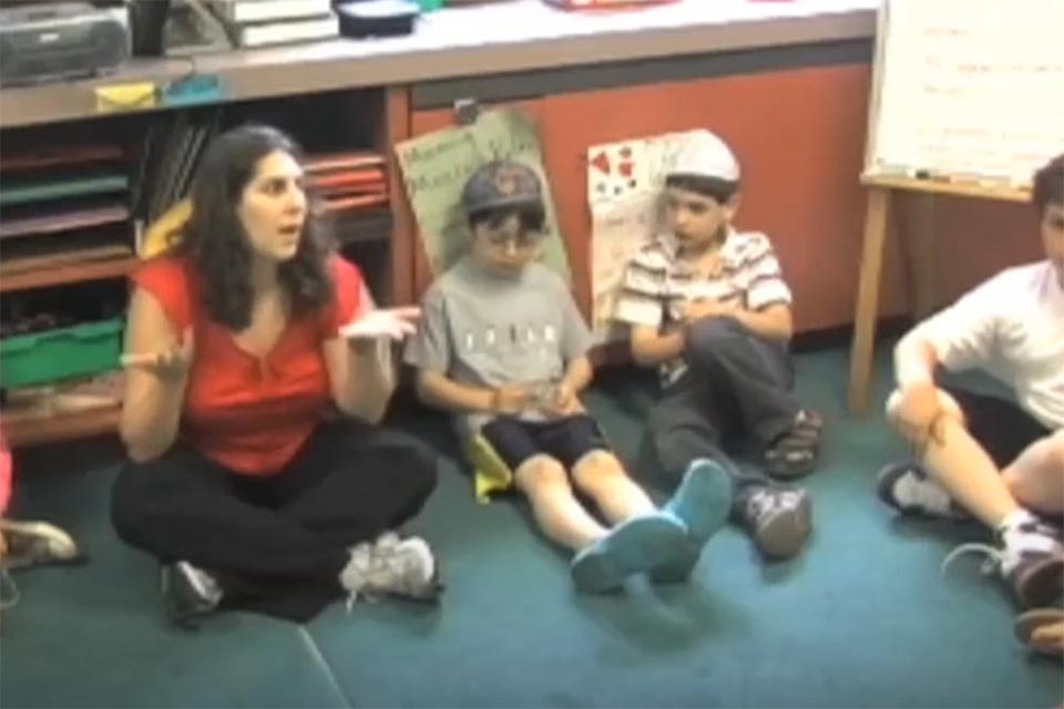 Jocelyn sits with her students on the rug engaged in a discussion.