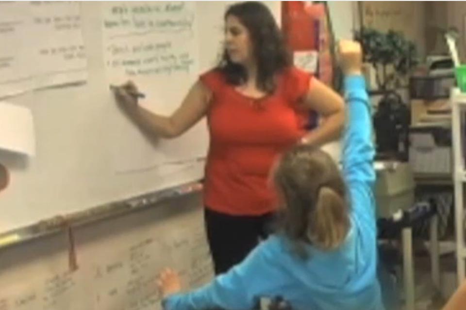 Jocelyn is standing at the white board, writing down the children's contributions to the discussion.