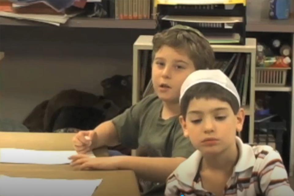 Picture of two boys seated at their desks, one of whom is talking about active listening.