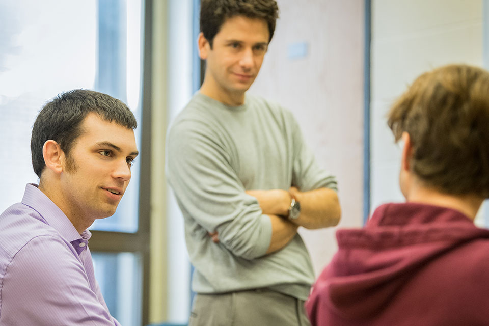 Two students talk, while a professor looks on