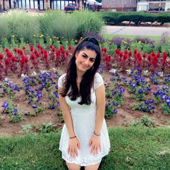 Jasmin smiling at the camera in front of red, yellow, and purple flowers