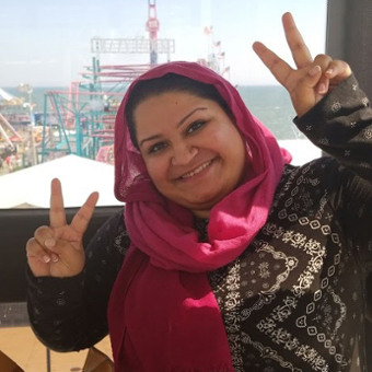 A picture of Maliha Chaudhry, on a ferris wheel, happily giving the peace sign with both hands, like a BOSS