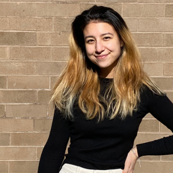 Sammie wearing a black long sleeve shirt, smiling at the camera, with her right hand on her hip